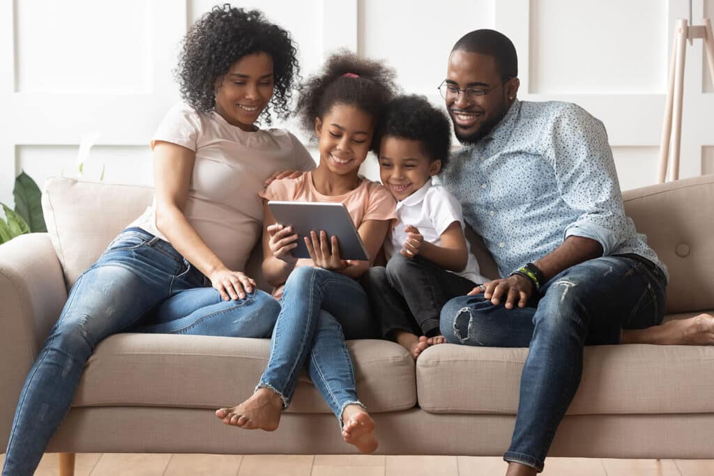 smiling family sitting on a couch looking at a tablet