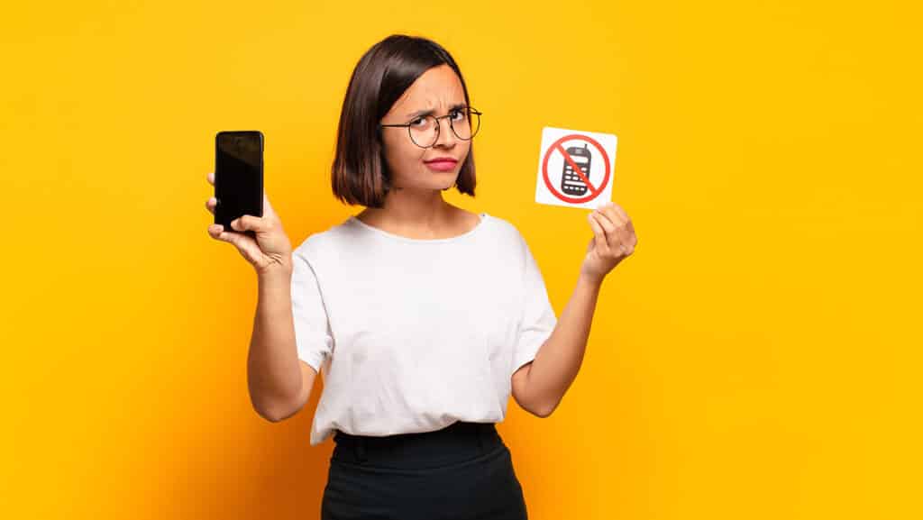 incredulous girl holding a cellphone and sign that says no cell phones