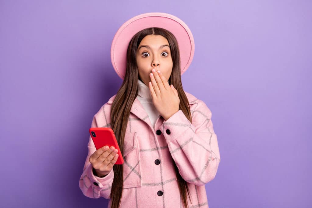 girl wearing pick looking shocked holding cell phone