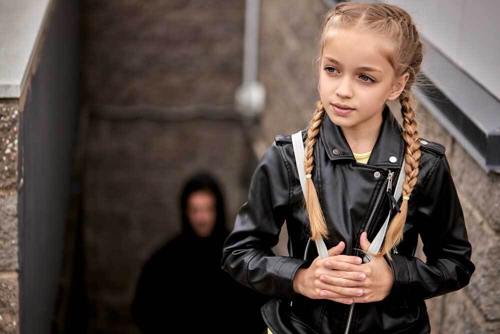 scary man in hood behind young girl who doesnt see him