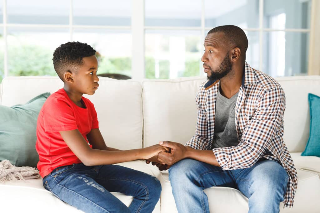 a father speaking seriously to his son while holding hands