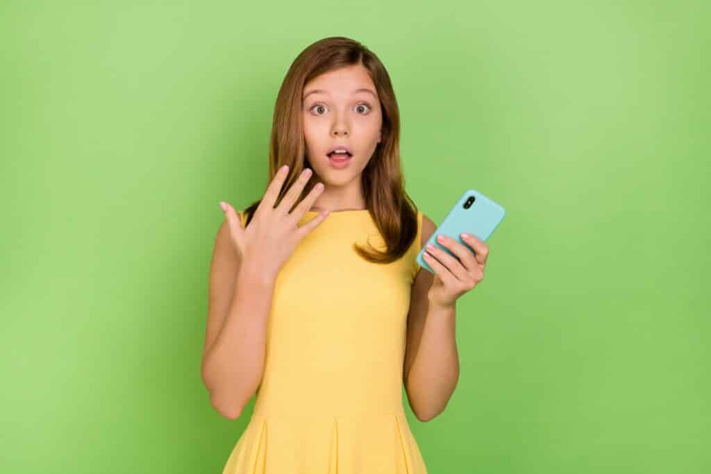 young girl holding cellphone with shocked expression