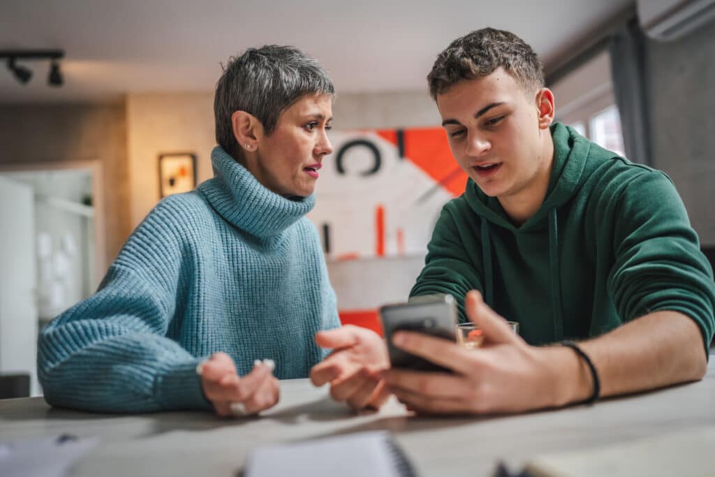 teen boy talking to his mother while looking at cellphone