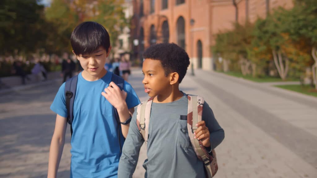 two little boys in backpacks walking away from school