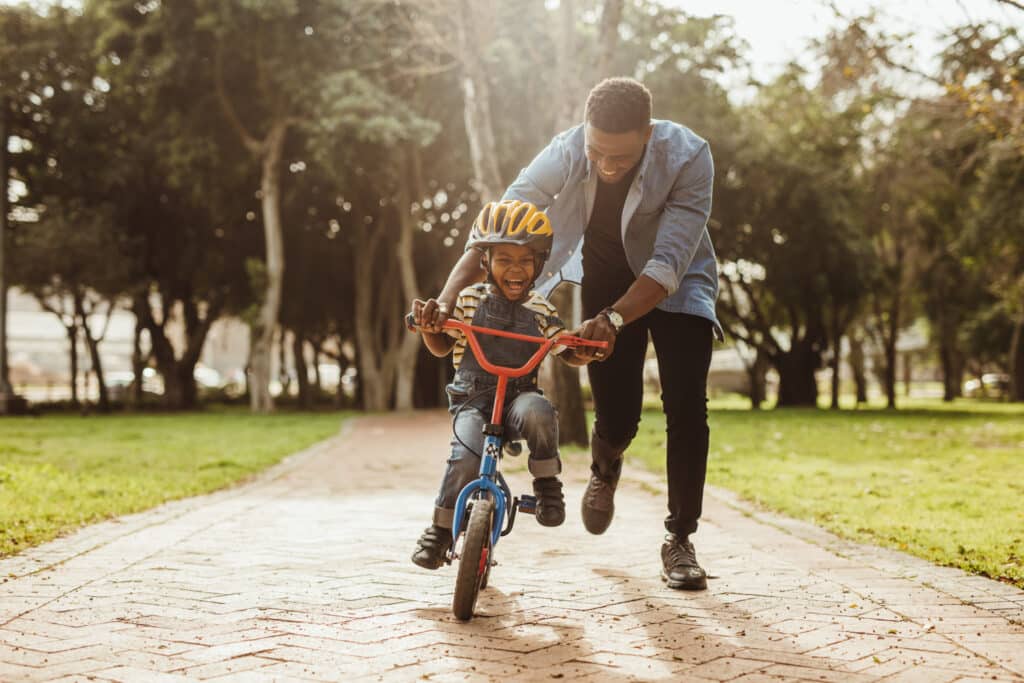 smiling father teaching happy son how to ride a bike