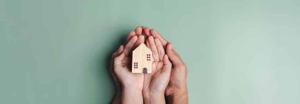 family of hands holding a wooden house