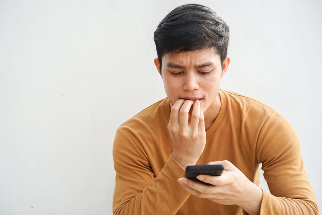 teen boy biting his nails while looking at his phone