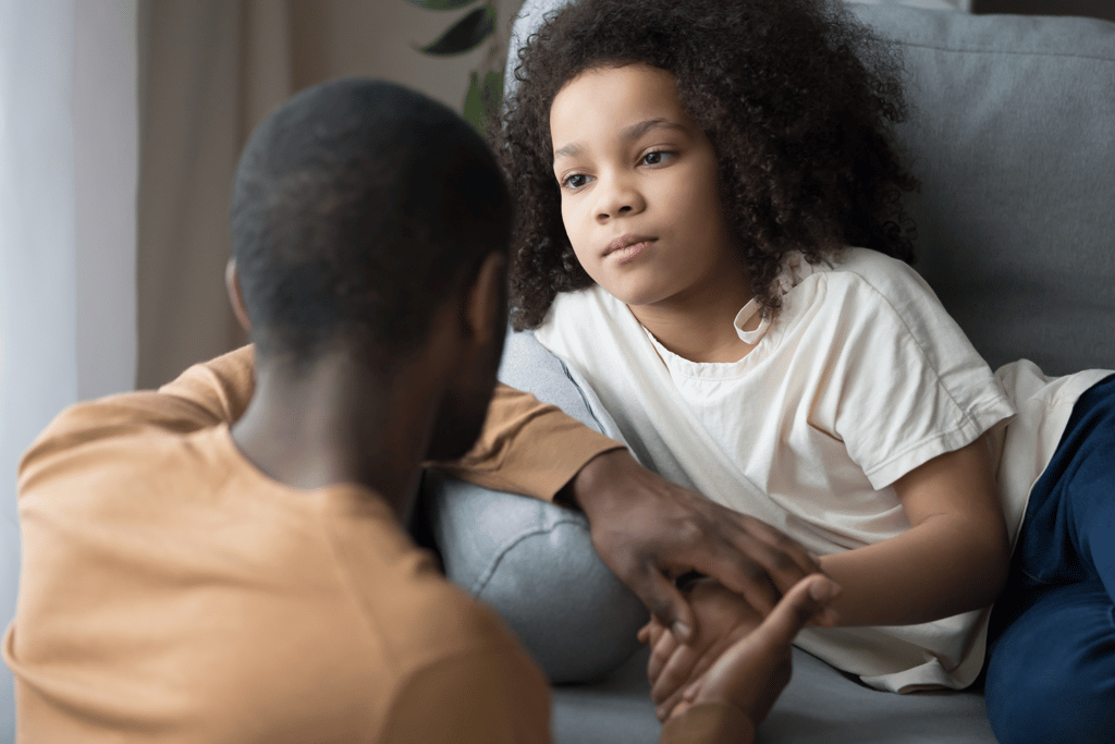 father looking at his young daughter on the couch holding hands