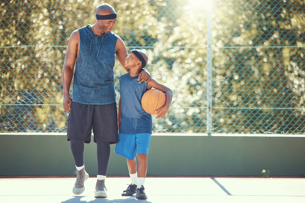 father and son smiling at each other playing basketball