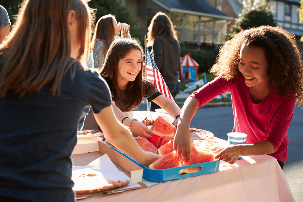 young girls smiling together as they reach for watermelon slices